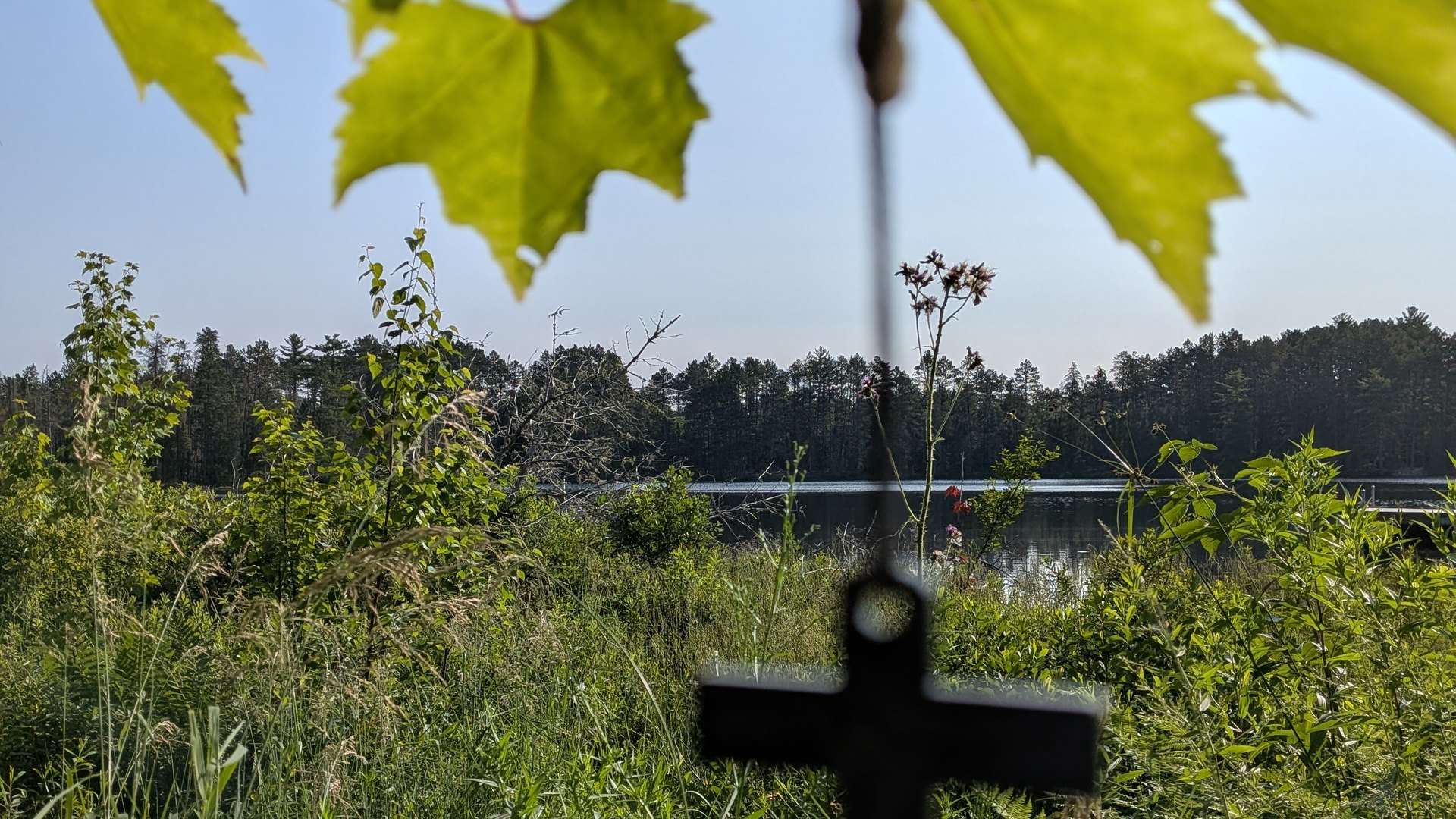 A hanging cross among maple leaves, with Nesbit Lake beyond